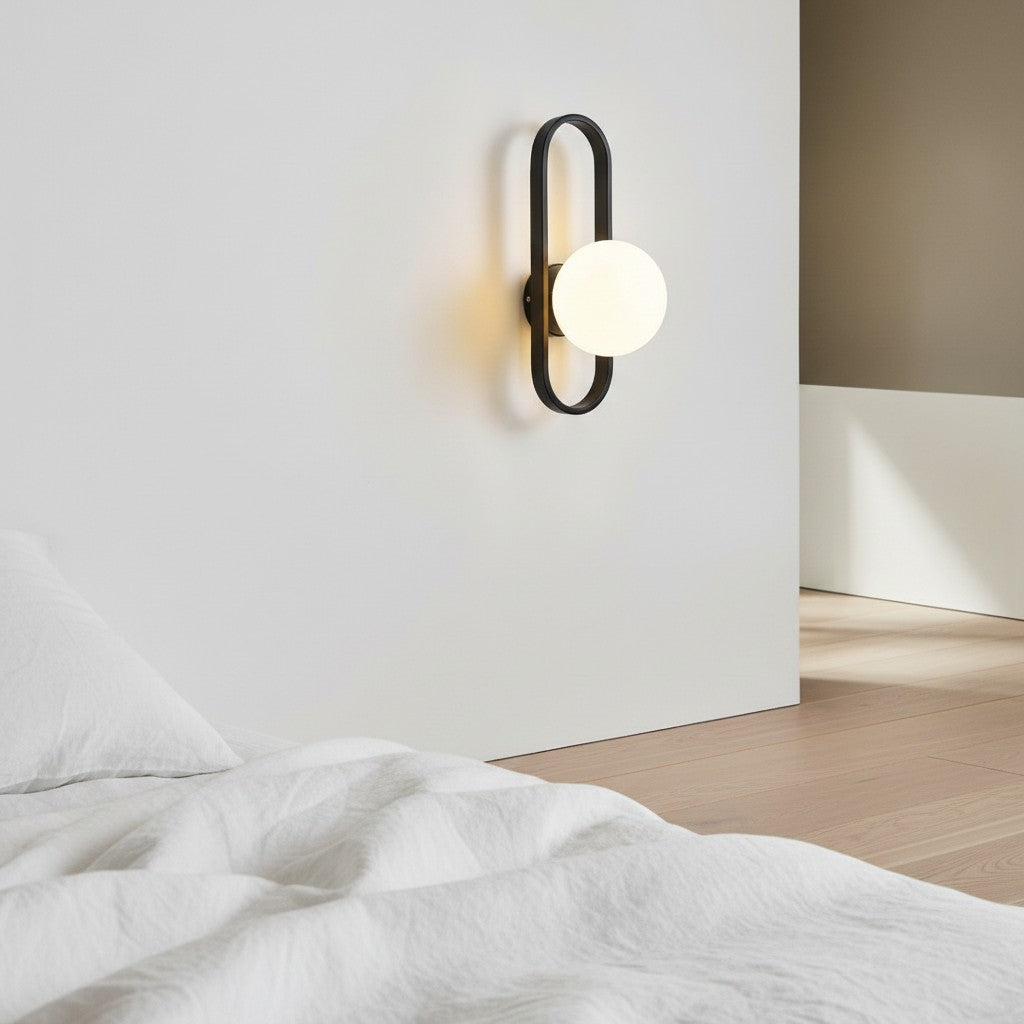 GoldenWatt luxury LED wall sconce with a black oval frame and glowing frosted glass globe shade in a modern bedroom.
