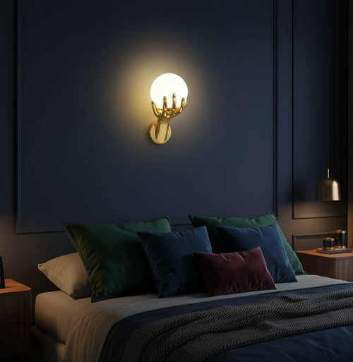 GoldenWatt gold hand-shaped wall sconce holding a glowing frosted glass orb light in a modern dark bedroom