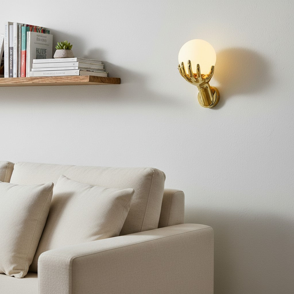 GoldenWatt gold hand-shaped wall lamp holding a glowing frosted glass orb light above a beige sofa in a modern living room.