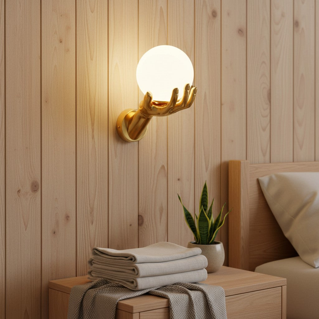GoldenWatt gold hand-shaped wall lamp holding a glowing frosted glass orb light fixture in a modern bedroom.
