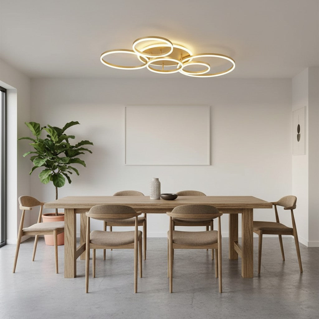 GoldenWatt modern gold LED ring chandelier illuminating a minimalist dining room with wooden furniture and a large plant