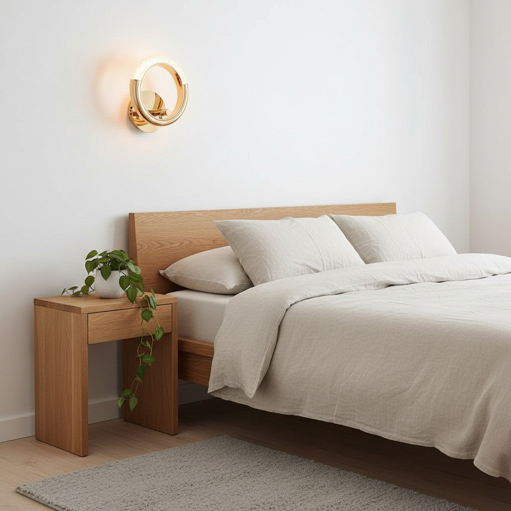 GoldenWatt Nordic gold circular LED wall lamp mounted above a wooden bedside table in a minimalist bedroom.