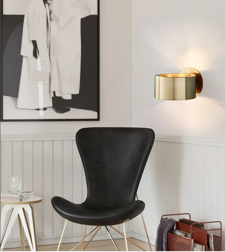 GoldenWatt Nordic gold iron wall sconce emitting warm white light in a modern living room with a black accent chair.